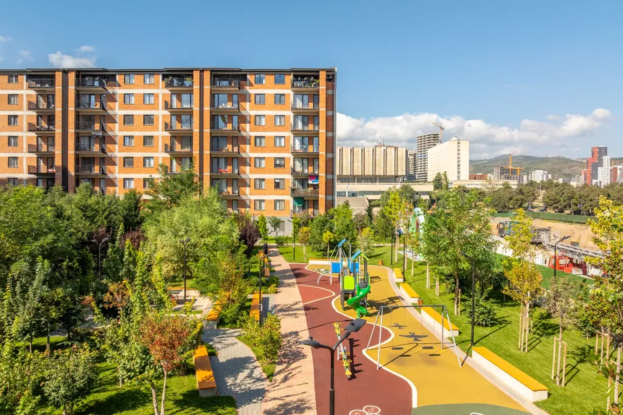 საცხოვრებელი კორპუსები საბავშვო სკვერის ზემოთ; მიღმა ქალაქის მაღლივი შენობები.